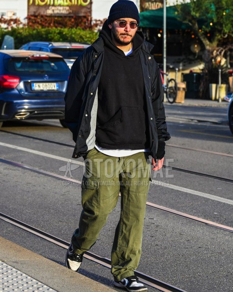 Men's fall/winter coordinate and outfit with solid navy knit cap, solid brown sunglasses, solid black windbreaker, solid black hoodie, solid white t-shirt, solid olive green cargo pants, and Nike Dunk black low-cut sneakers.