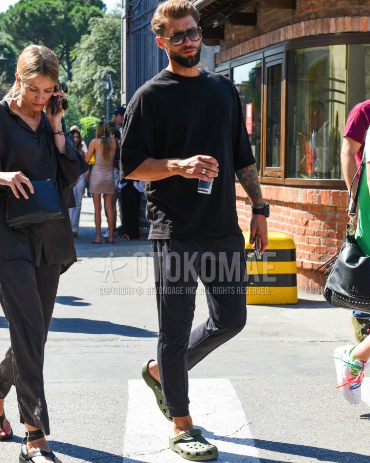 Summer/spring men's coordinate and outfit with dark gray tortoiseshell sunglasses, plain black t-shirt, dark gray plain jogger pants/ribbed pants, and olive green sandals.