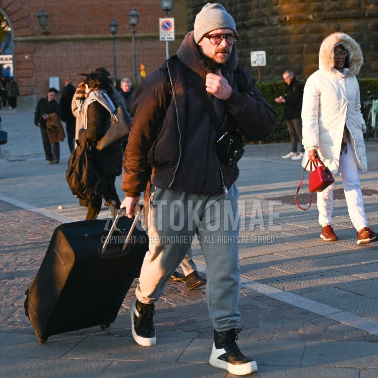 Men's fall/winter coordinate and outfit with plain gray knit cap, brown tortoiseshell glasses, plain black down jacket, dark gray plain hoodie, plain gray sweatpants, and black, white, and multi-colored high-cut sneakers.