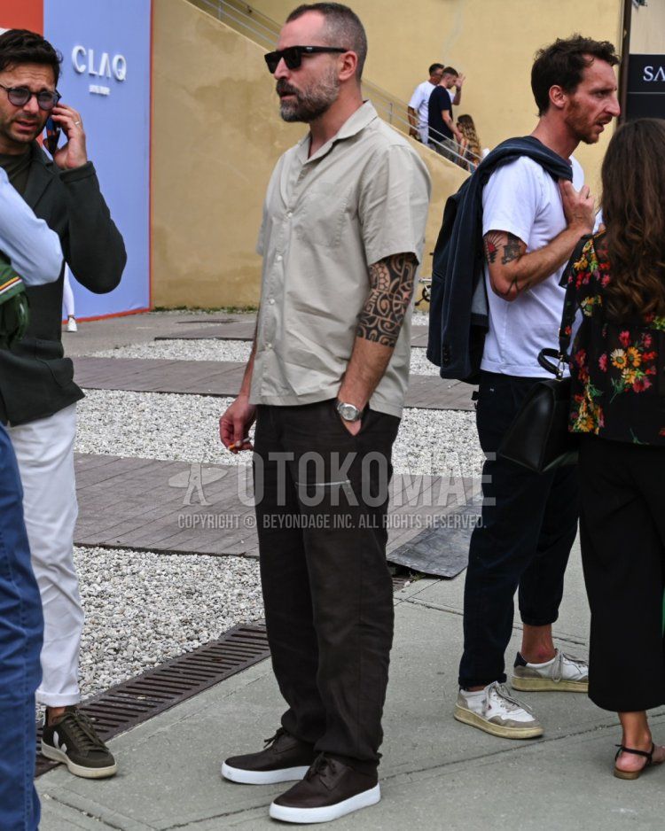 Men's spring/summer coordinate and outfit with plain black sunglasses, plain beige shirt, plain black jogger pants/ribbed pants, and brown low-cut sneakers.