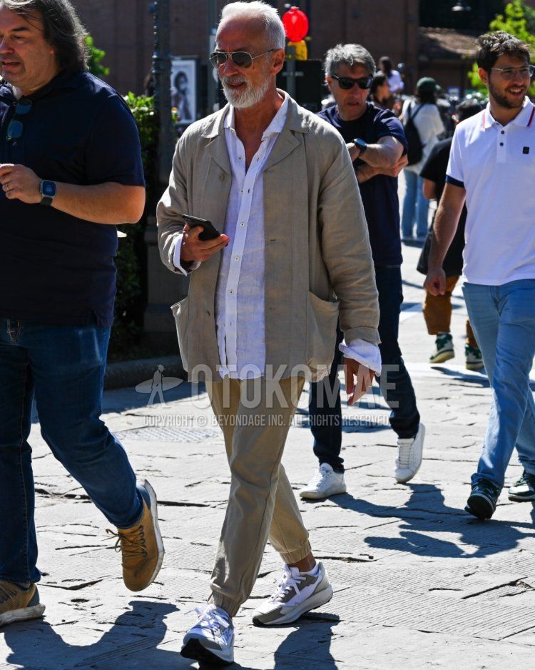 Men's fall/summer/spring outfit with plain black sunglasses, plain beige coveralls, plain white t-shirt, plain beige jogger pants/ribbed pants, and white low-cut sneakers.
