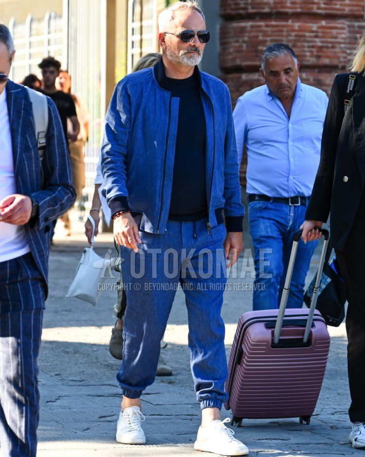 Men's fall/summer/spring outfit with solid black sunglasses, solid blue MA-1, solid black t-shirt, solid blue jogger pants/ribbed pants, and white low-cut sneakers.