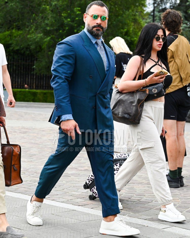 Men's fall/summer/spring outfit with solid green sunglasses, solid light blue denim/chambray shirt, white low-cut sneakers, solid blue suit, and white dot tie.