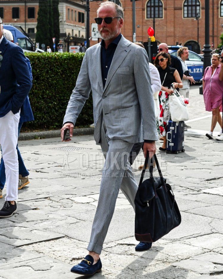 Men's spring/summer/fall outfit with plain black sunglasses, plain navy shirt, navy bit loafer leather shoes, plain navy briefcase/handbag, and plain gray suit.