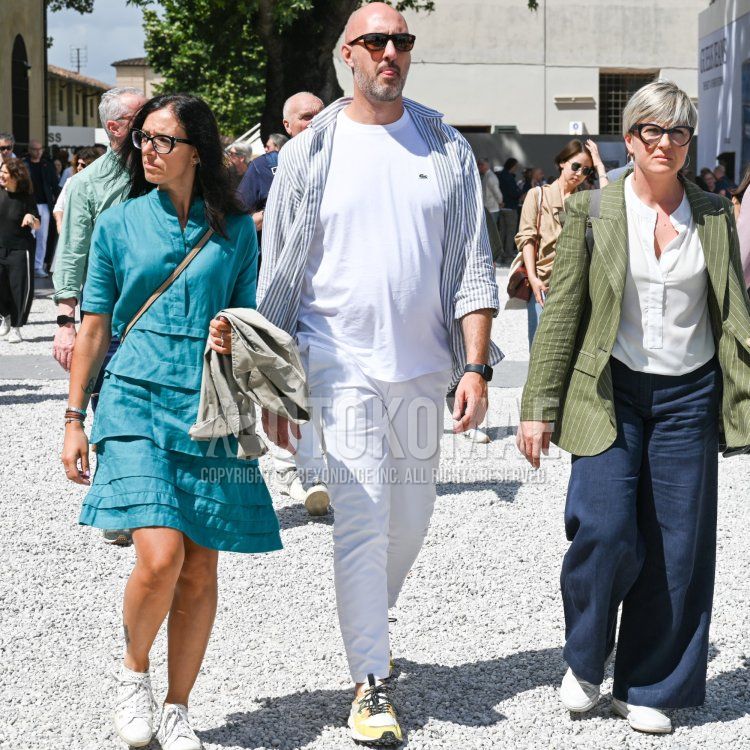 黒無地のサングラス、グレー・白ストライプのシャツ、白無地のTシャツ、白無地のチノパン、白・イエロー・黒ローカットのスニーカーを合わせた秋春のメンズコーデ・着こなし。