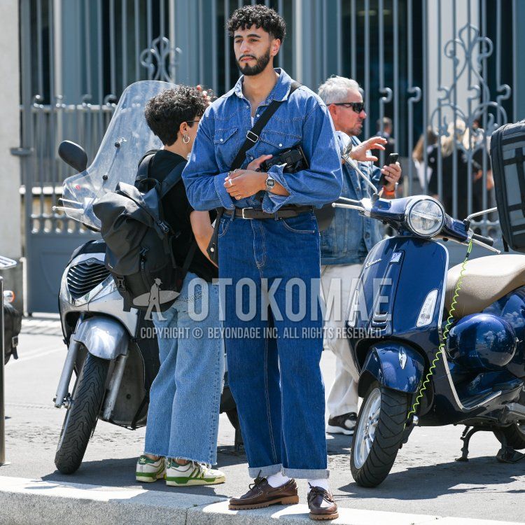 Men's spring/summer coordinate and outfit with plain blue shirt, plain brown leather belt, plain blue denim/jeans, brown moccasin/deck shoes leather shoes, and plain black shoulder bag.