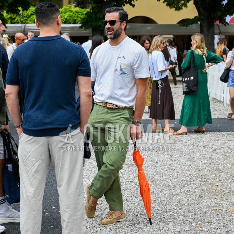 Men's spring/summer coordinate and outfit with plain black sunglasses, white lettered t-shirt, beige leather belt, plain green baker pants, and beige moccasin/deck shoe leather shoes.