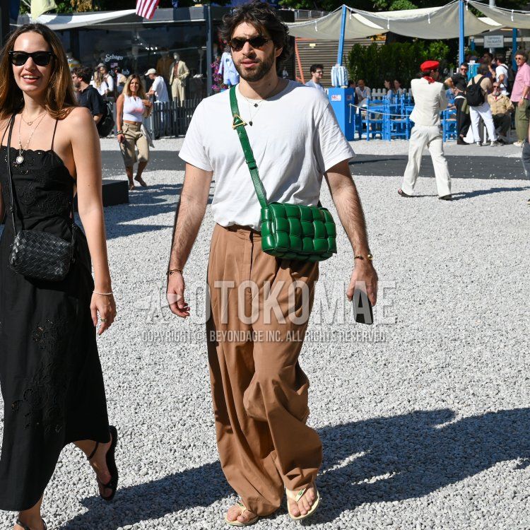 Summer/spring men's coordinate and outfit with brown tortoiseshell sunglasses, plain white t-shirt, plain brown slacks, plain brown pleated pants, yellow flip flops, and leather green plain shoulder bag.