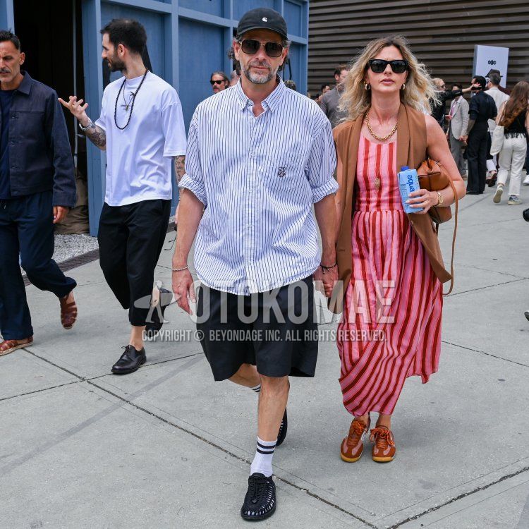 Men's summer coordinate and outfit with black one-pointed baseball cap, solid gold sunglasses, white striped shirt, solid black shorts, white socks, and Keen black sandals.