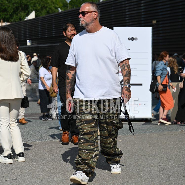 Men's spring/summer coordinate and outfit with brown tortoiseshell sunglasses, plain white t-shirt, multi-colored camouflage cargo pants, and white low-cut sneakers.