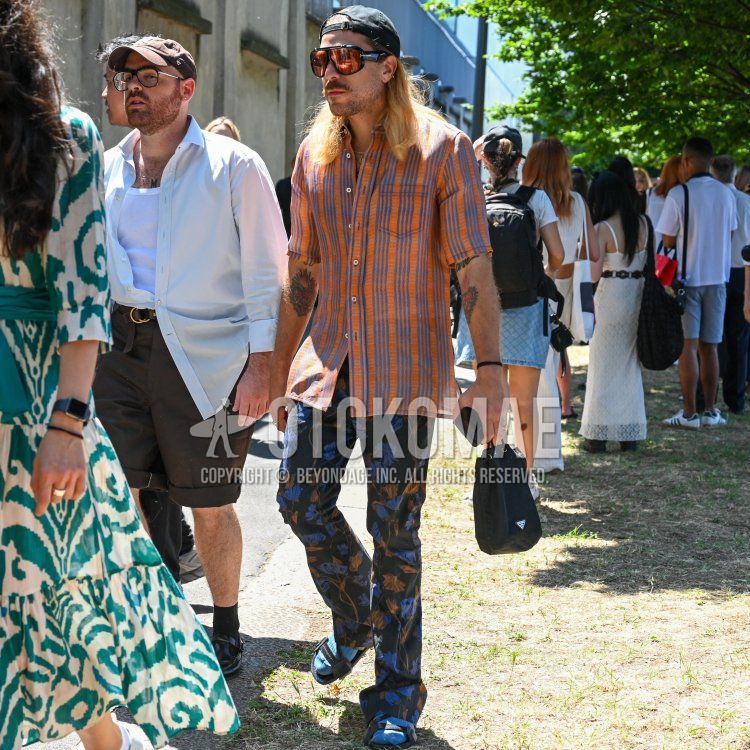 Men's summer/spring outfit with plain black baseball cap, plain black Tom Ford sunglasses, orange checked shirt, all black slacks, plain light blue socks, black leather sandals, and plain black Prada bag.