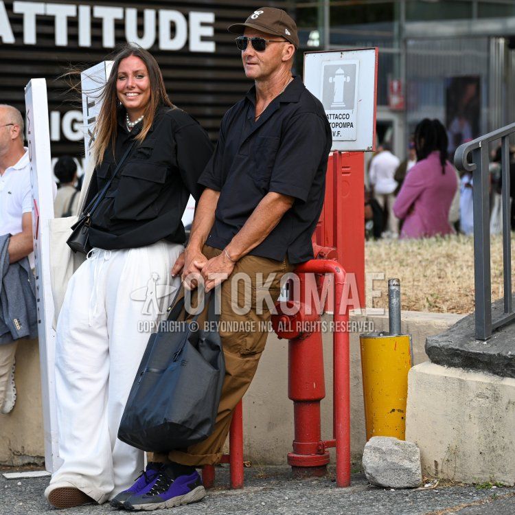 Men's summer/spring outfit with New Era brown lettered baseball cap, plain silver/black sunglasses, plain black polo shirt, plain brown cargo pants, Nike purple low-cut sneakers, and plain gray briefcase/handbag.