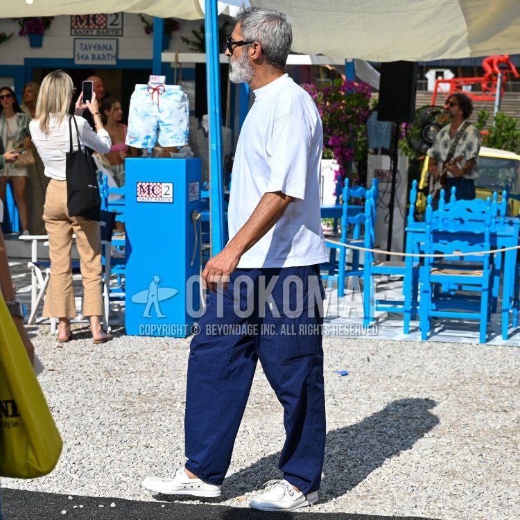 Men's spring/summer coordination and outfit with plain black glasses, plain white T-shirt, plain blue/navy cargo pants, and white moccasins/deck shoes leather shoes.