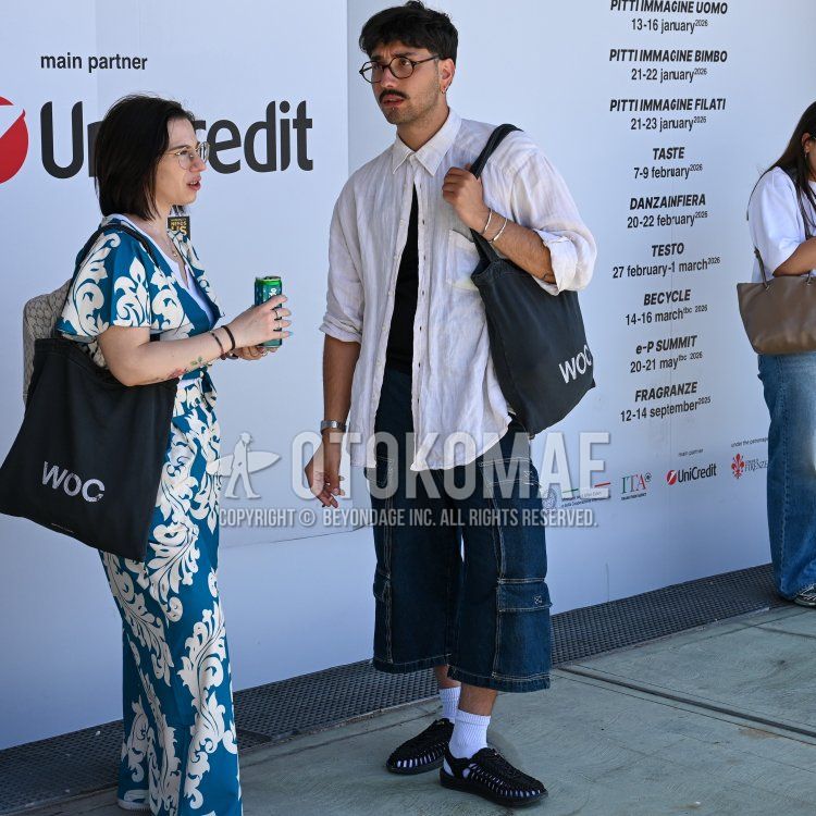 Men's summer/spring outfit with brown tortoiseshell glasses, plain white shirt, plain black t-shirt, plain blue shorts, plain blue denim/jeans, plain white socks, Keen Unique black sandals, and black lettered tote bag.