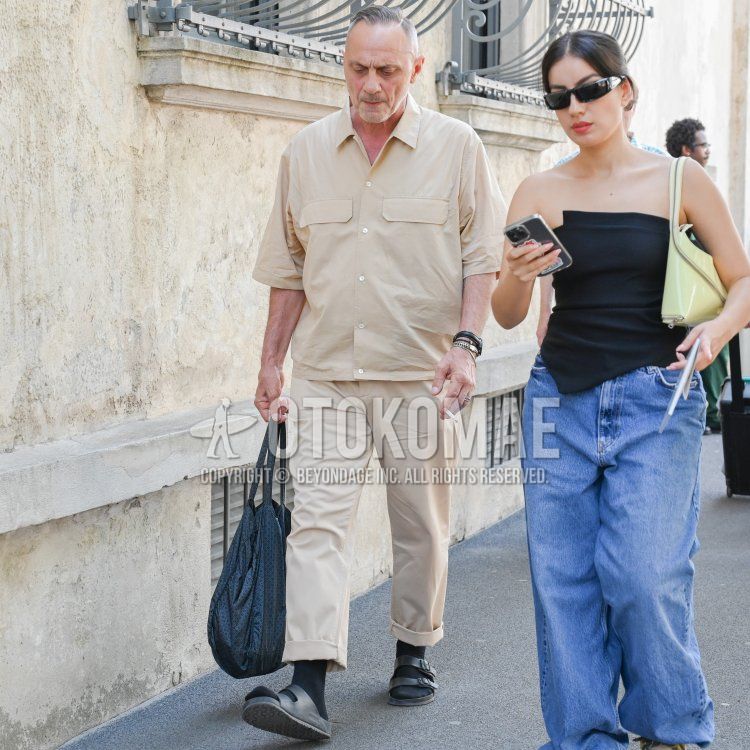 Men's spring/summer coordinate and outfit with plain beige shirt, plain beige chinos, plain black socks, black leather sandals, and black small print tote bag.
