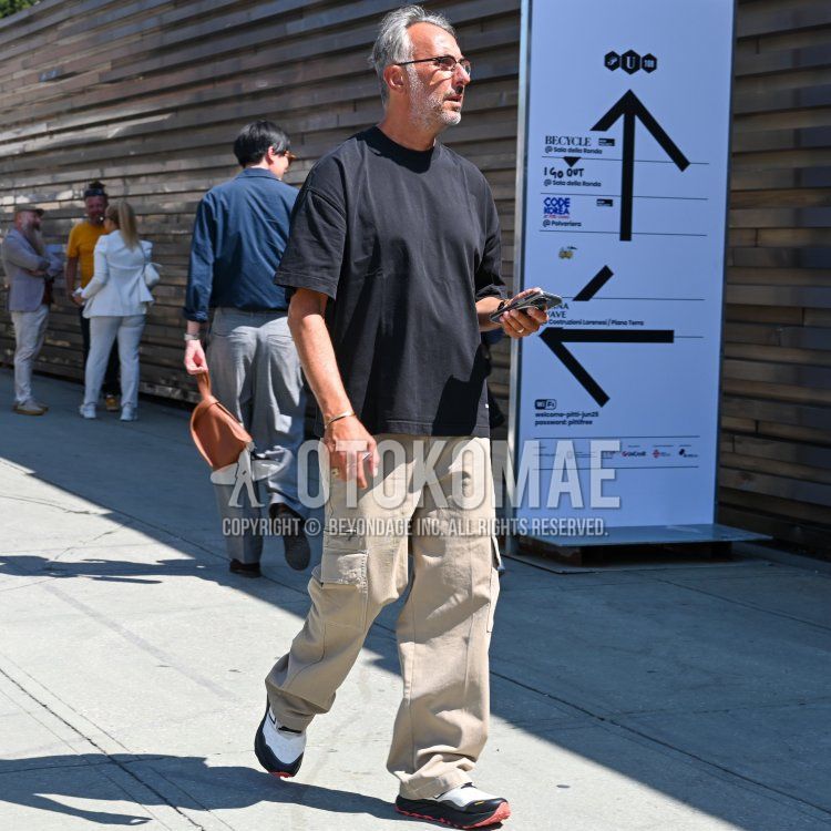 Summer/spring men's coordinate and outfit with plain black glasses, plain black t-shirt, plain beige cargo pants, plain beige chinos, and white low-cut sneakers.