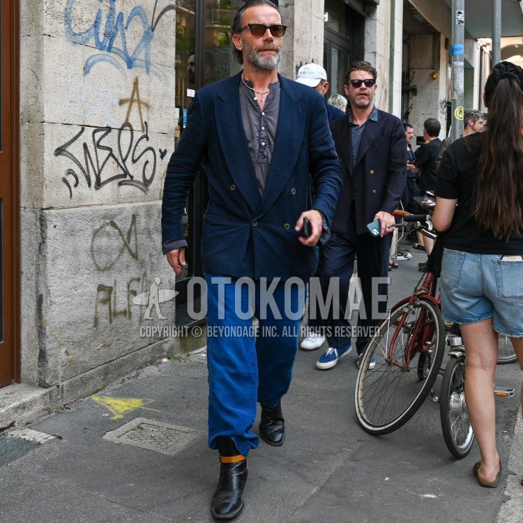 A summer/spring men's outfit and outfit with plain black sunglasses, plain navy tailored jacket, plain gray shirt with band collar henley neck, plain blue chinos, and black boots.
