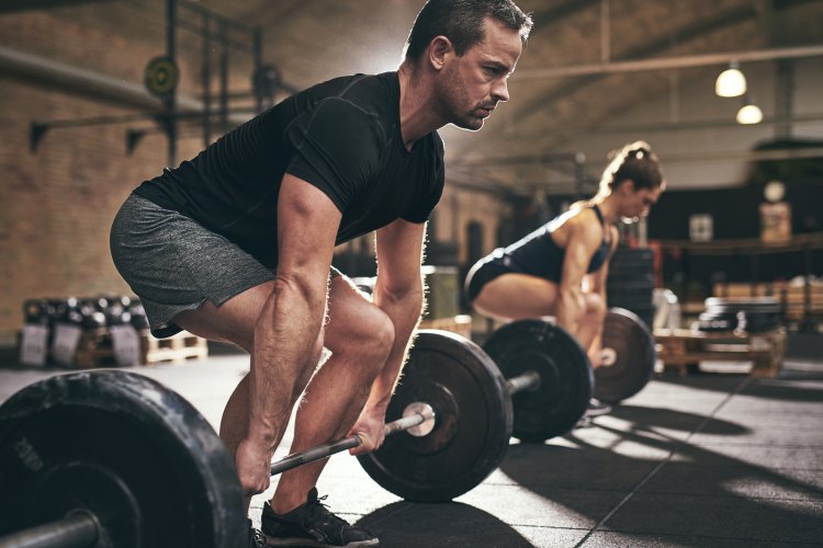 Spotive man and woman lifting heavy barbells