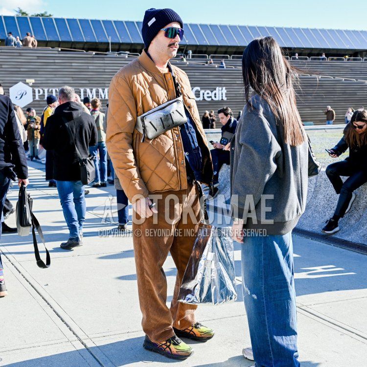 Solid navy knit cap, solid blue sunglasses, solid beige MA-1, solid beige quilted jacket, solid brown winter pants (corduroy, velour), Asics yellow/orange low cut sneakers, Valentino gray decal logo shoulder bag by Valentino.