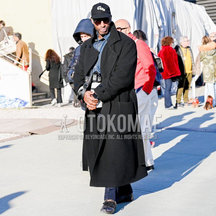 Men's fall/winter coordinate and outfit with black one-point baseball cap, solid black sunglasses, solid black belted coat, solid blue denim jacket, solid navy slacks, and black low-cut New Balance sneakers.
