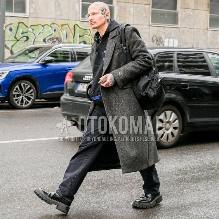 Men's fall/winter coordinate/outfit with plain silver glasses, plain dark gray chester coat, Comme des Garcons black deca logo hoodie, plain black denim/jeans, black side gore boots, and plain black backpack.