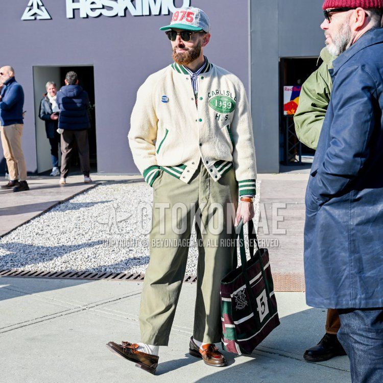 Gray lettered baseball cap, brown tortoiseshell sunglasses, plain white stadium jacket, white striped shirt, olive green plain chinos, olive green plain ankle pants, plain white socks, brown tassel loafer leather shoes, red and Olive green lettered tote bag for men in fall and winter.