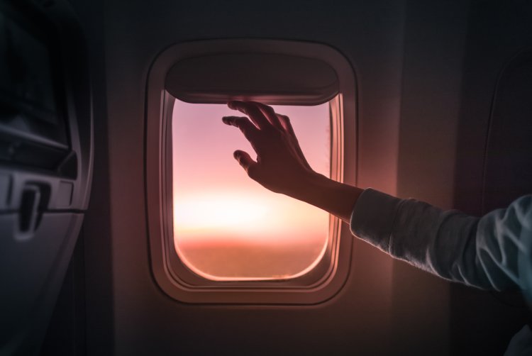 Female's hand opening airplane window at sunset.
