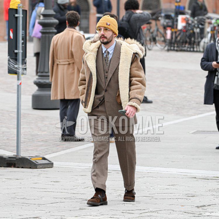 Winter men's coordination and outfit with solid orange knit cap, solid gray glasses, solid brown boa jacket/coat, solid light blue shirt, brown loafer leather shoes, solid brown suit, and yellow/black checked tie.