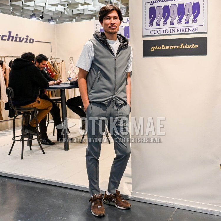 Men's fall/spring outfit with plain gray casual vest, plain white t-shirt, plain gray slacks, plain gray easy pants, and New Balance 991 brown low-cut sneakers.