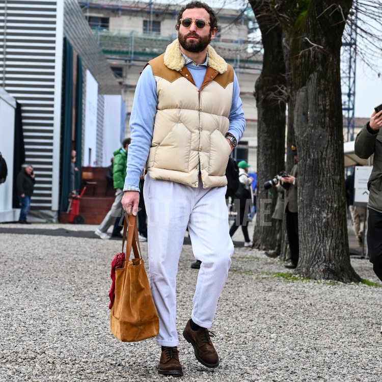 ベージュのダウンベストに、水色のニットとストライプシャツを重ね、白のコーデュロイパンツを合わせた男性。3月上旬の春の素材感を取り入れた着こなし。