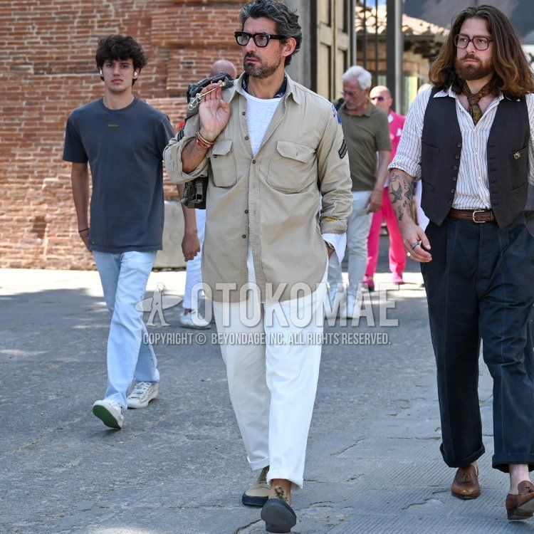 Spring men's coordinate and outfit with plain black glasses, navy paisley bandana/neckerchief, plain beige shirt jacket, plain white t-shirt, plain beige chinos, beige low-cut sneakers, and plain beige backpack.