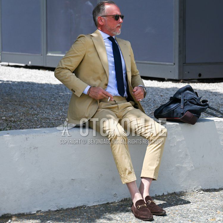 Men's spring/summer outfit with olive green solid color sunglasses, blue solid color shirt, brown bit loafer leather shoes, yellow solid color suit and black solid color tie.
