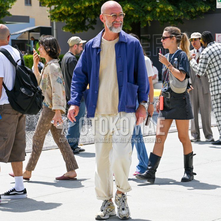 Men's spring/summer coordinate and outfit with solid yellow sunglasses, solid purple/navy shirt jacket, solid beige t-shirt, solid white slacks, and white low-cut sneakers.