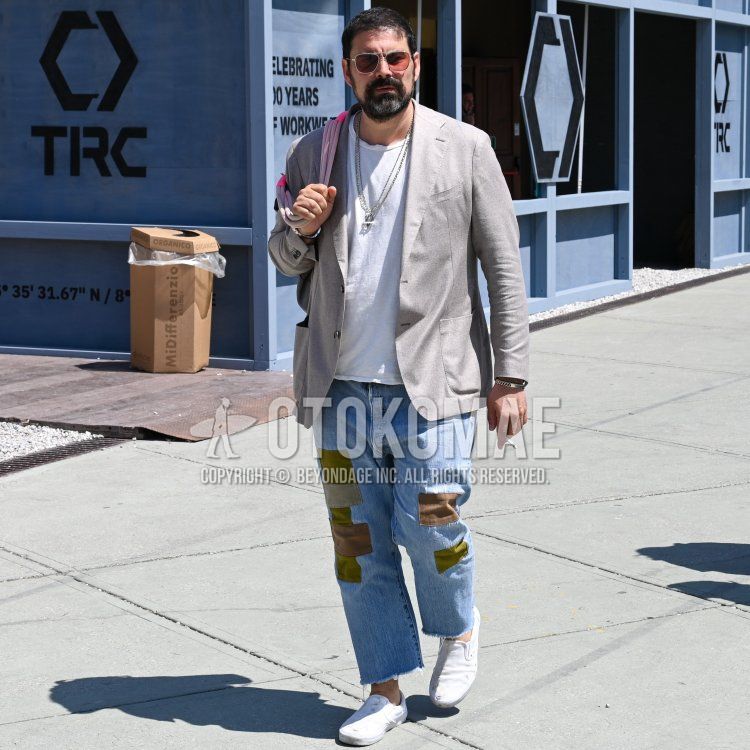 Summer/spring men's coordinate/outfit with teardrop solid silver sunglasses, solid gray tailored jacket, solid white t-shirt, solid blue denim/jeans, solid blue ankle pants, solid white slip-on sneakers, solid pink tote bag.