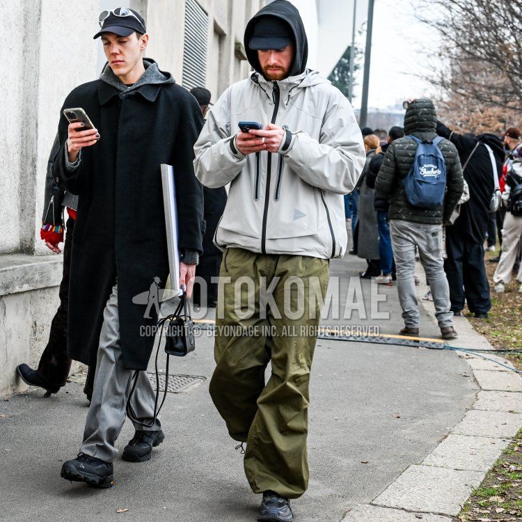 Men's winter/spring/fall outfit with solid navy baseball cap, solid gray windbreaker, solid black hoodie, solid olive green easy pants, and black low-cut sneakers.