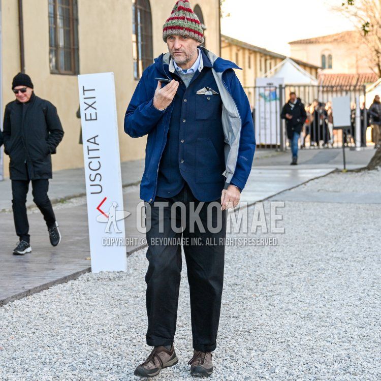 Men's fall/spring/winter outfit with solid beige/red knit cap, solid blue windbreaker, solid navy cardigan, solid gray sweater, solid light blue shirt, solid black slacks, and brown low-cut sneakers.