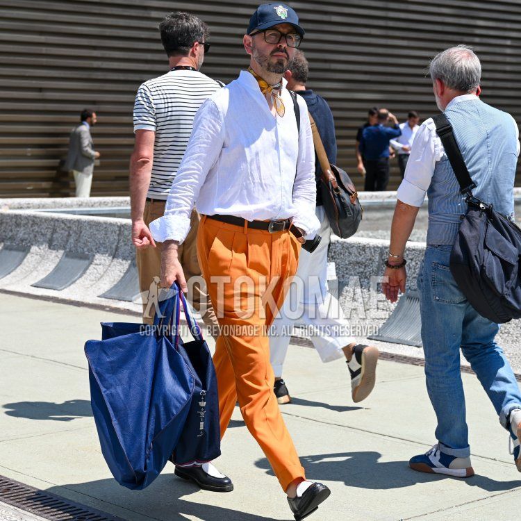 Navy one-pointed baseball cap, plain black glasses, multi-colored stole bandana/neckerchief, plain white shirt, plain black leather belt, plain orange slacks, plain orange pleated pants, plain white/black loafer leather shoes, plain blue briefcase/ Men's spring/summer outfit/coordination with handbag.