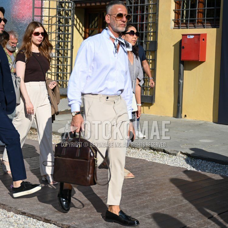 Teardrop gold plain sunglasses, white/black stole bandana/neckerchief, plain white shirt, plain beige ankle pants, plain beige slacks, plain beige beltless pants, coin loafer leather shoes, plain leather brown briefcase/handbag with a men's spring/summer outfit/coordination.