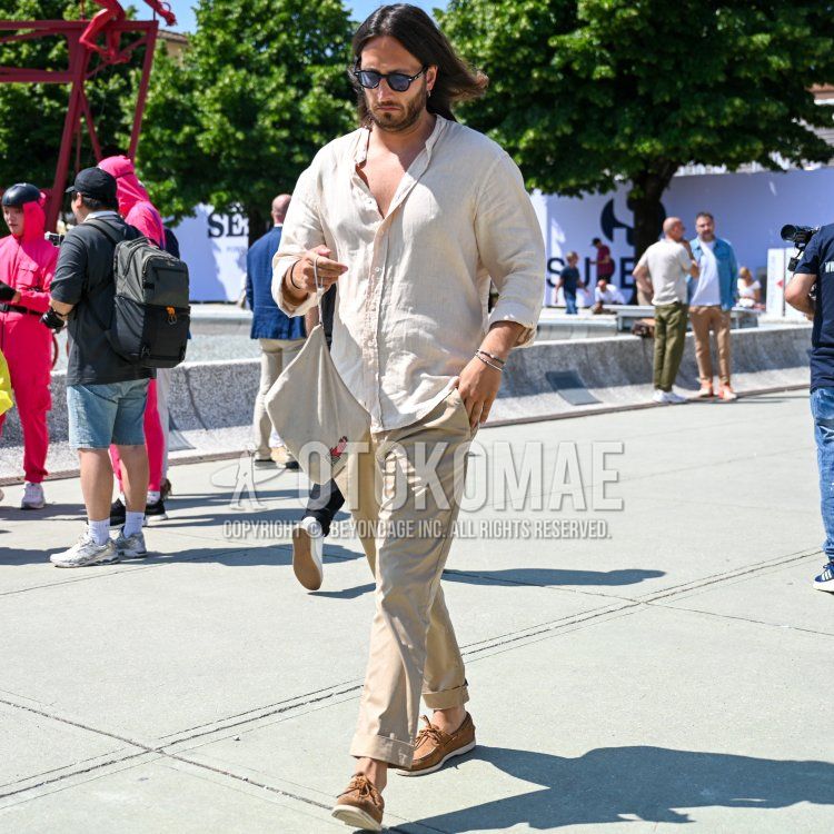 Summer/spring men's coordinate and outfit with plain black Wellington sunglasses, plain white shirt with band collar, plain beige chinos, brown moccasin/deck shoes leather shoes, brown suede shoes leather shoes, and plain white bag.