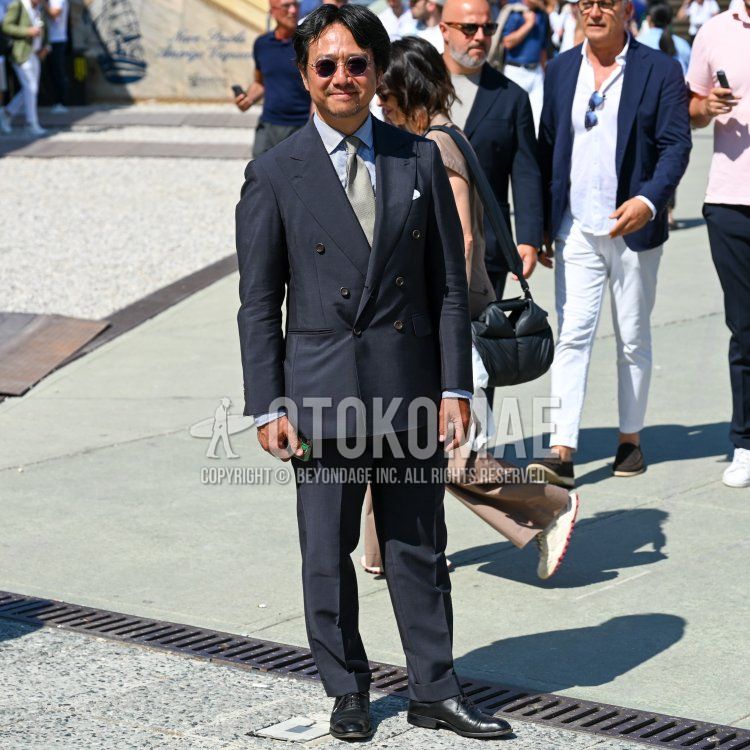 A spring/summer men's outfit featuring clear, solid-color sunglasses, a blue-and-white striped shirt, black straight-tip leather shoes, a solid black suit, and a gray tie.