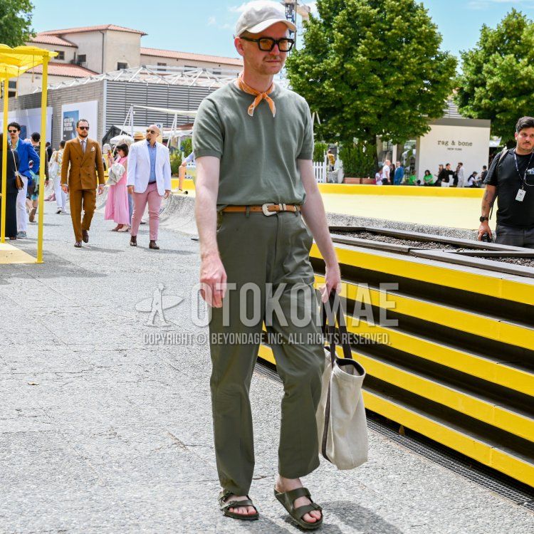 A summer men's outfit featuring a plain white baseball cap, plain black glasses, a plain orange scarf, a plain olive green T-shirt, a plain brown leather belt, plain olive green slacks, olive green leather sandals, and a plain white and olive green tote bag.