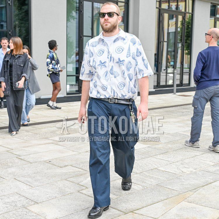 黒無地のサングラス、ブルー・白総柄のシャツ、黒無地のレザーベルト、ブルー無地のワイドパンツ、黒コインローファーの革靴を合わせた春夏のメンズコーデ・着こなし。