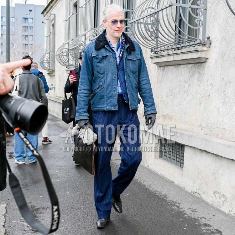 An autumn/winter men's outfit featuring teardrop-shaped solid silver sunglasses, a solid blue denim jacket, a solid light blue shirt, a solid blue down vest, blue-striped slacks, black plain-toe leather shoes, and a solid black briefcase/handbag.