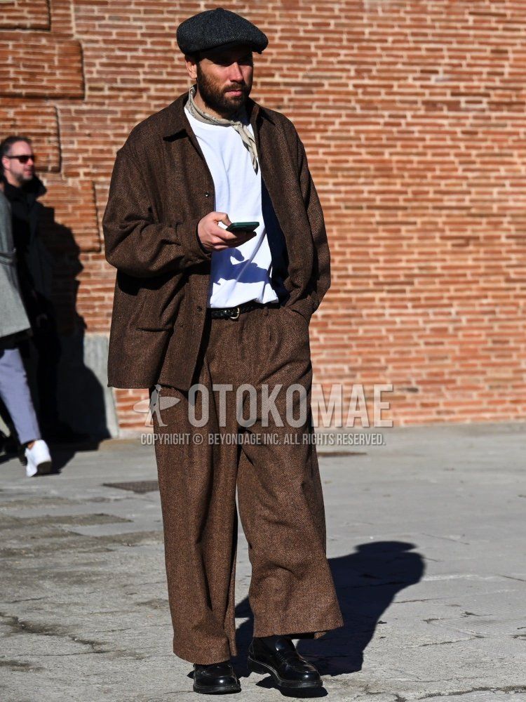 A men's outfit for fall, winter, and spring featuring a dark gray herringbone flat cap, a beige bandana/neckchief, a solid brown shirt jacket, a solid white long-sleeve T-shirt, a solid black leather belt, solid brown slacks, solid black socks, and black leather coin loafers.